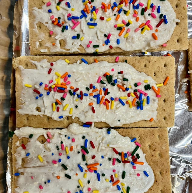 A dip that is composed of cream cheese, butter, grounded oats, and sugar is distributed across a graham cracker, and is garnished with sprinkles.